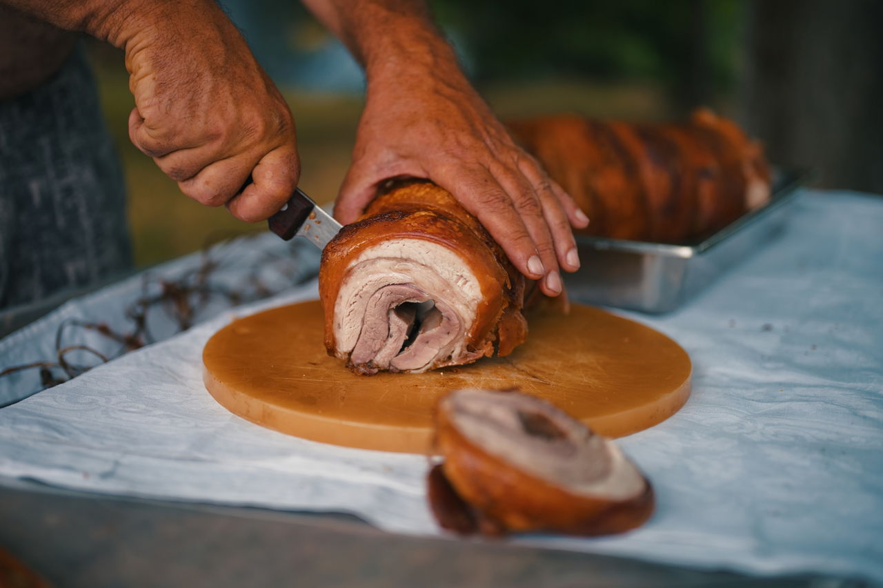 Cropped shot of hands cutting big piece of pork meat on the table in nature
