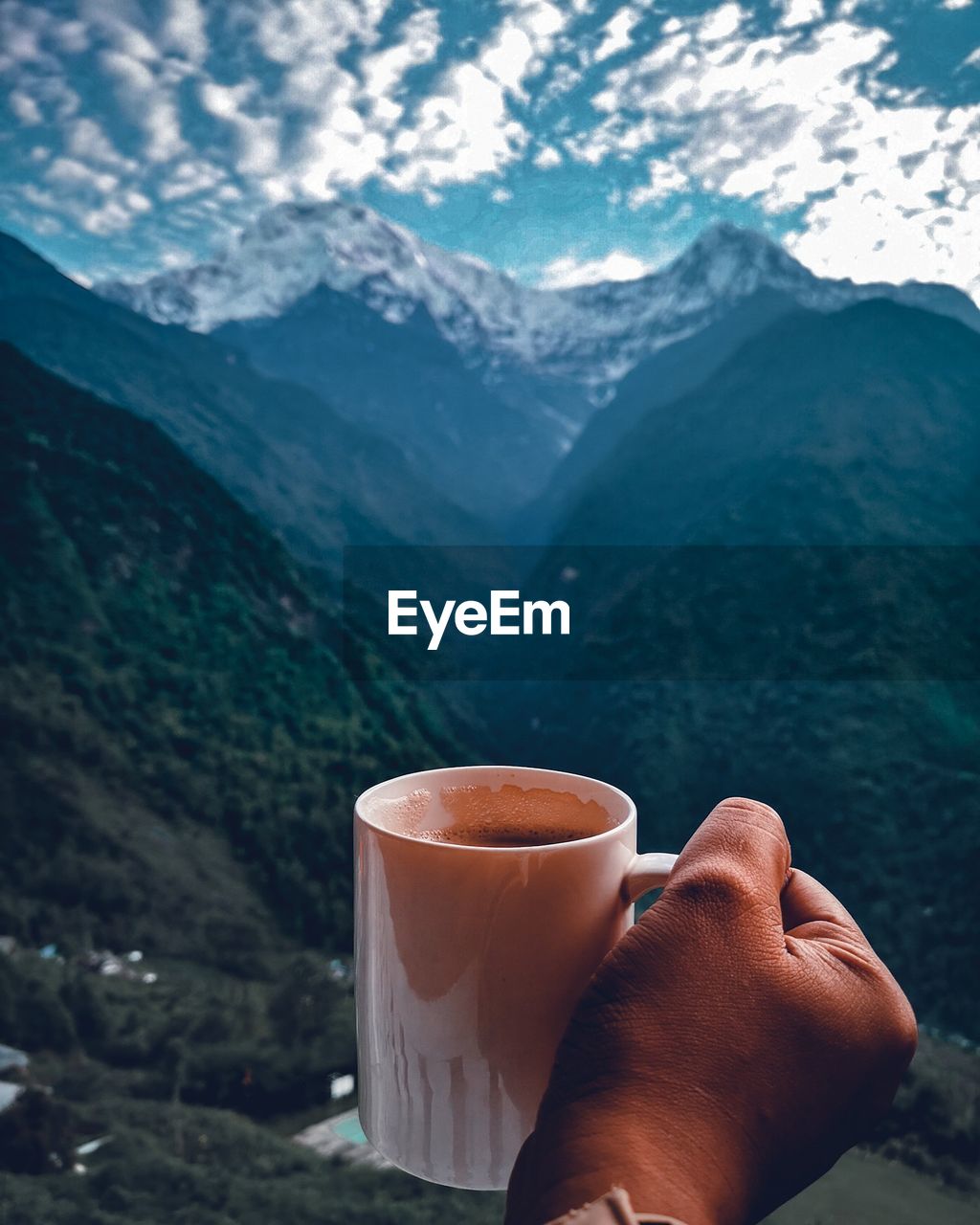 Cropped hand holding coffee mug against mountains