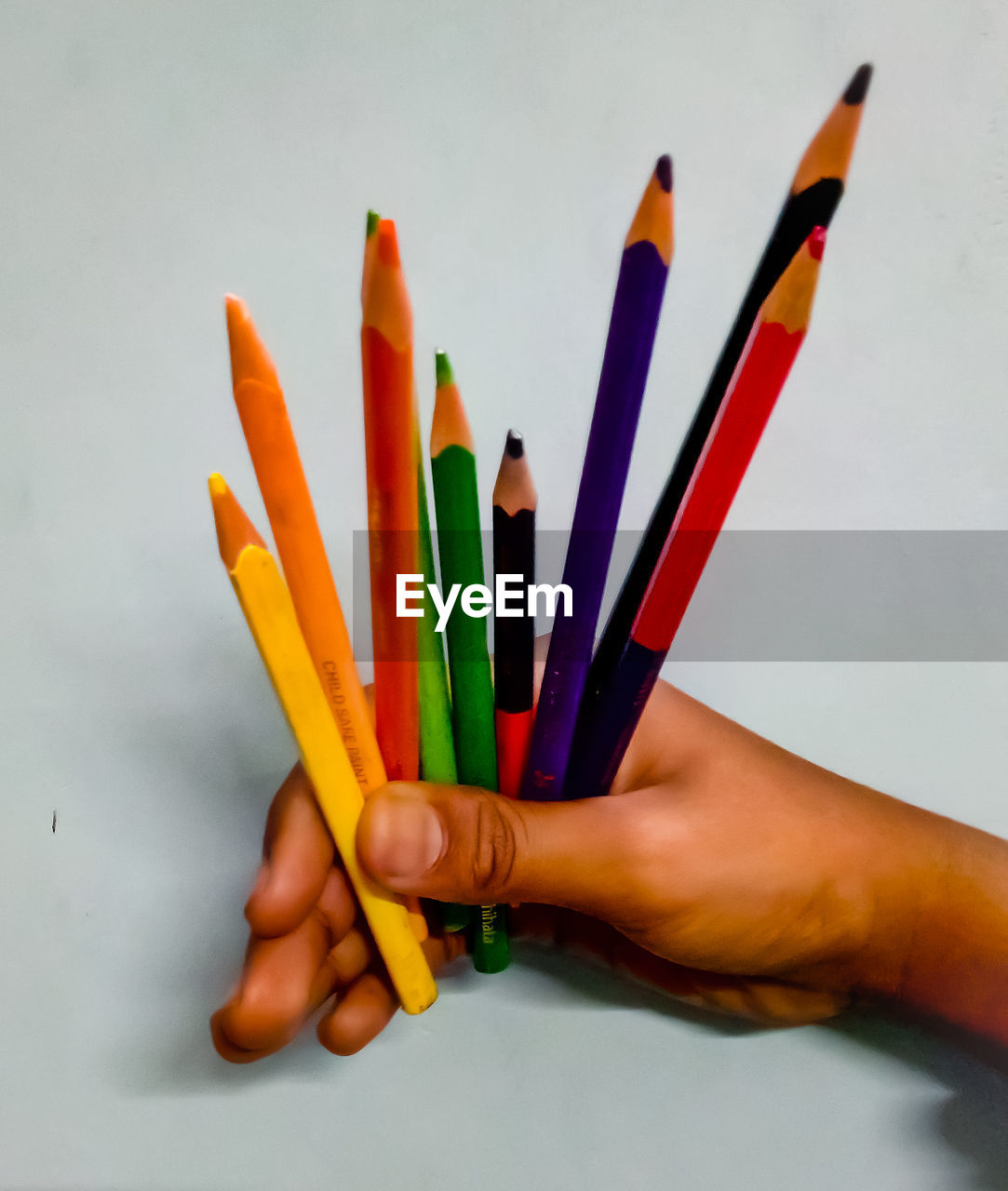 Close-up of hand holding colored pencils against white background