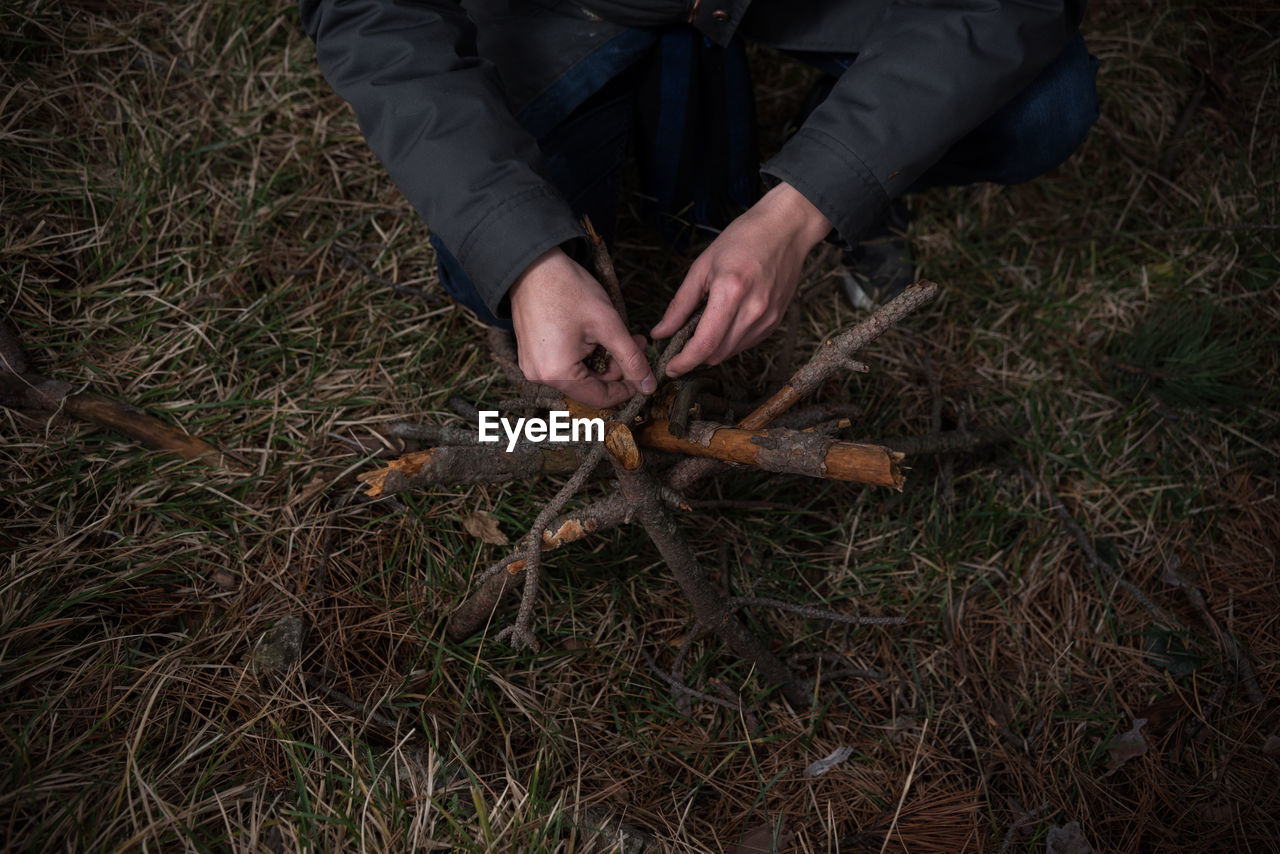 Cropped image of person arranging wooden sticks over grass field