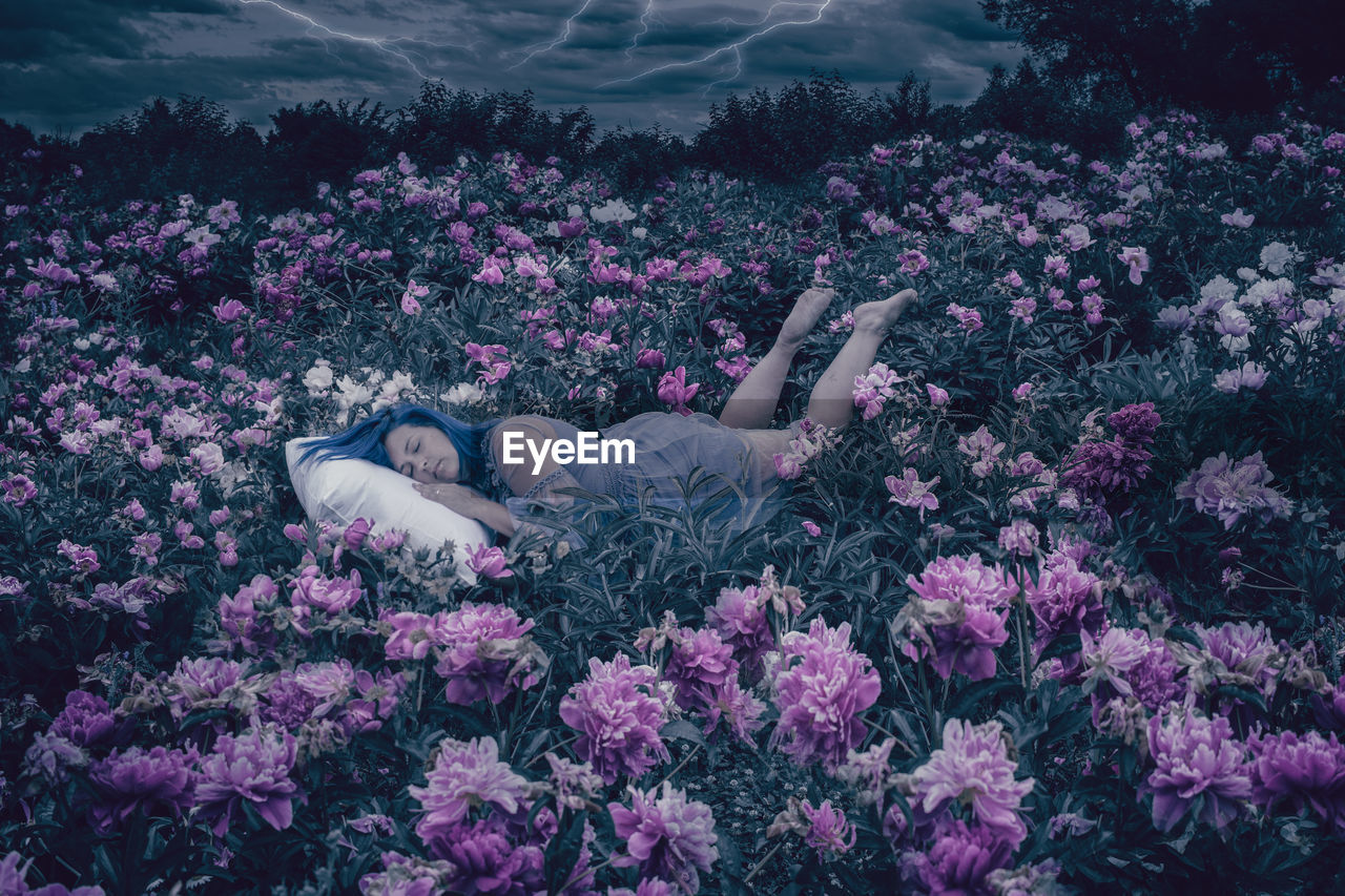 LOW SECTION OF PERSON LYING ON PURPLE FLOWERING PLANT