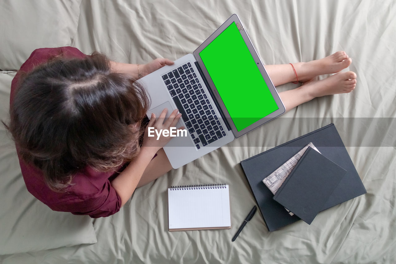 High angle view of woman using laptop while sitting on bed at home