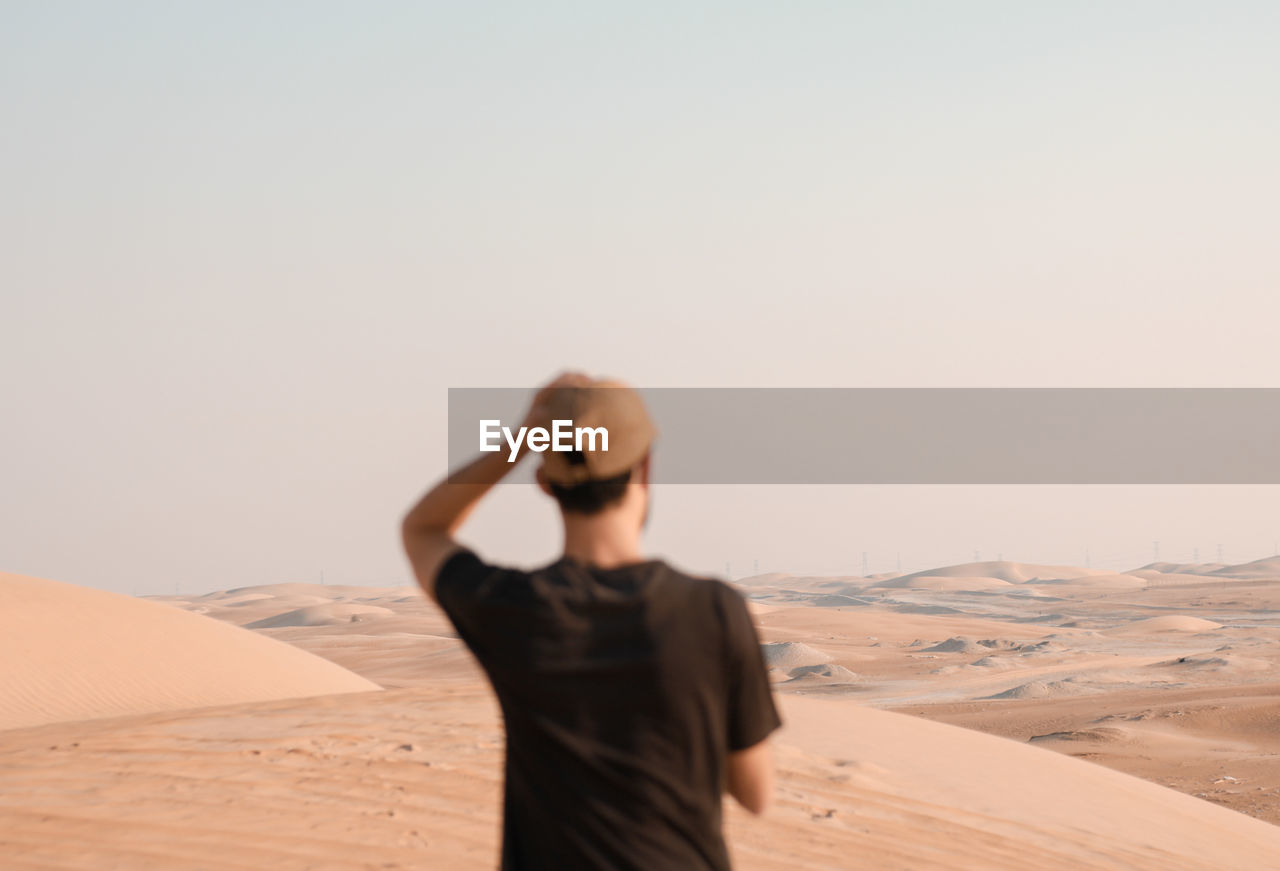 Young man on sand dune in desert against clear sky