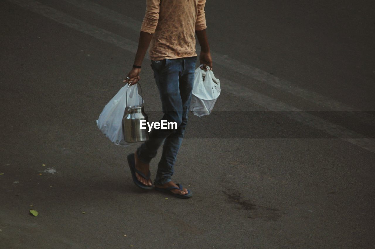 Low section of man carrying plastic bags while walking on road
