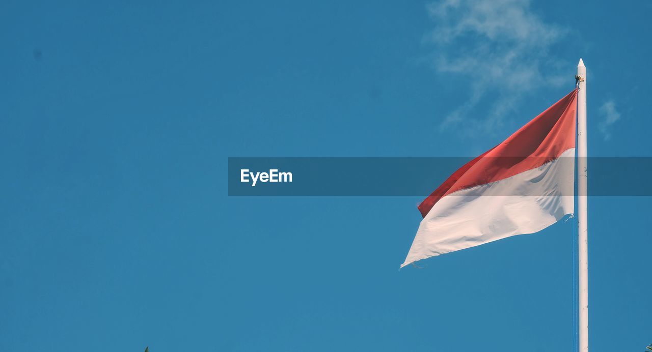 Low angle view of indonesian flag waving against blue sky