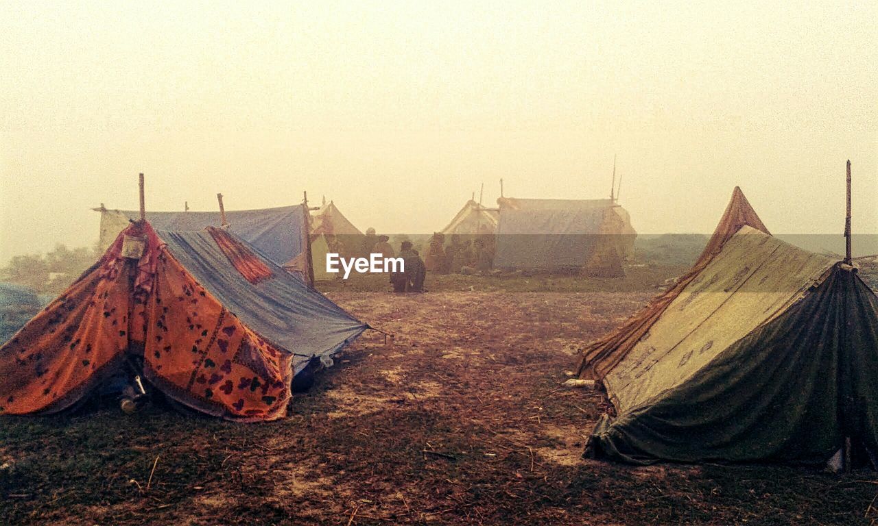 People on field by tents against clear sky during foggy weather