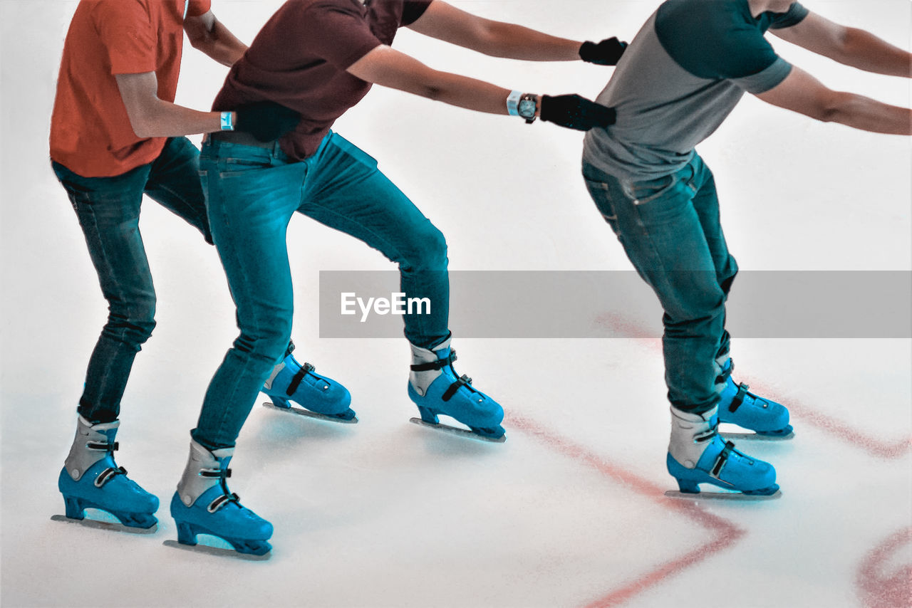 Low section of male friends ice-skating on rink