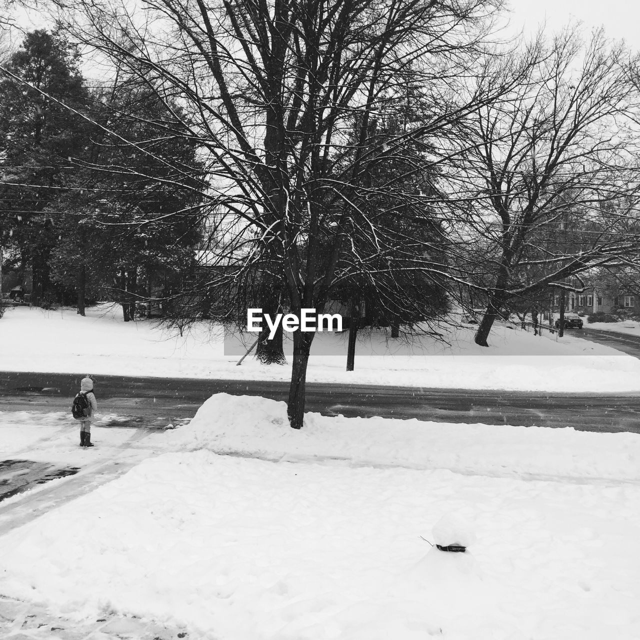 Rear view of kid standing on snow by street in winter