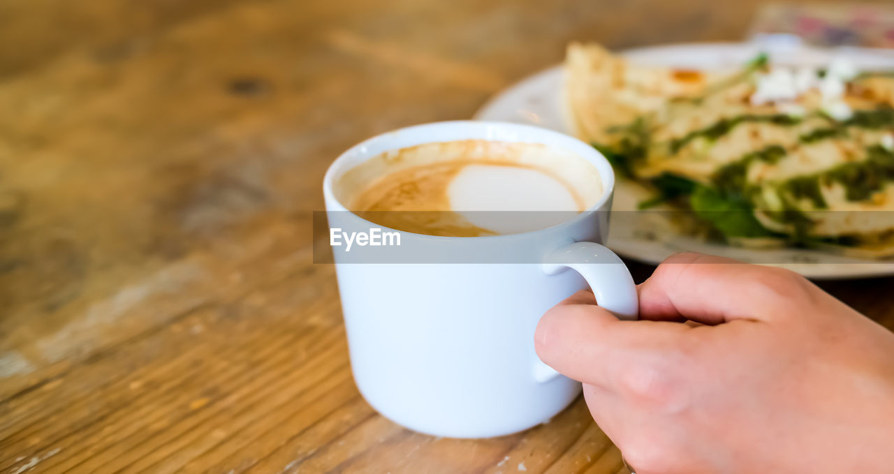 Cropped image of hand holding coffee cup on table