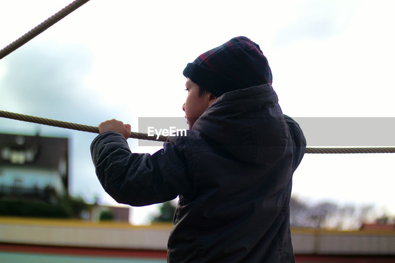 Rear view of boy standing by rope against sky