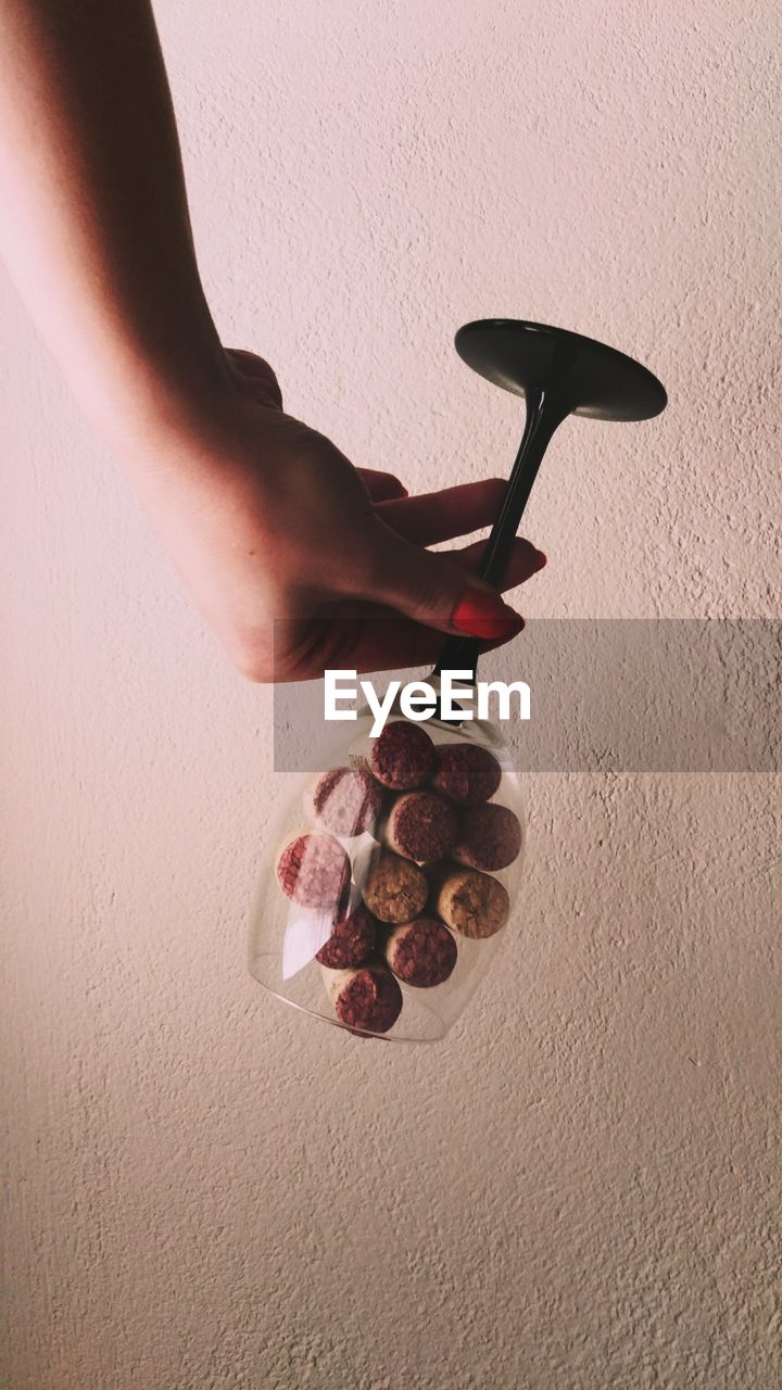 Upside down image of woman holding wineglass with corks against wall