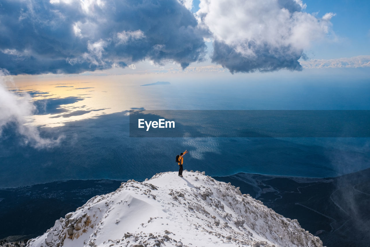 Man looking at sea by snowcapped mountain against sky
