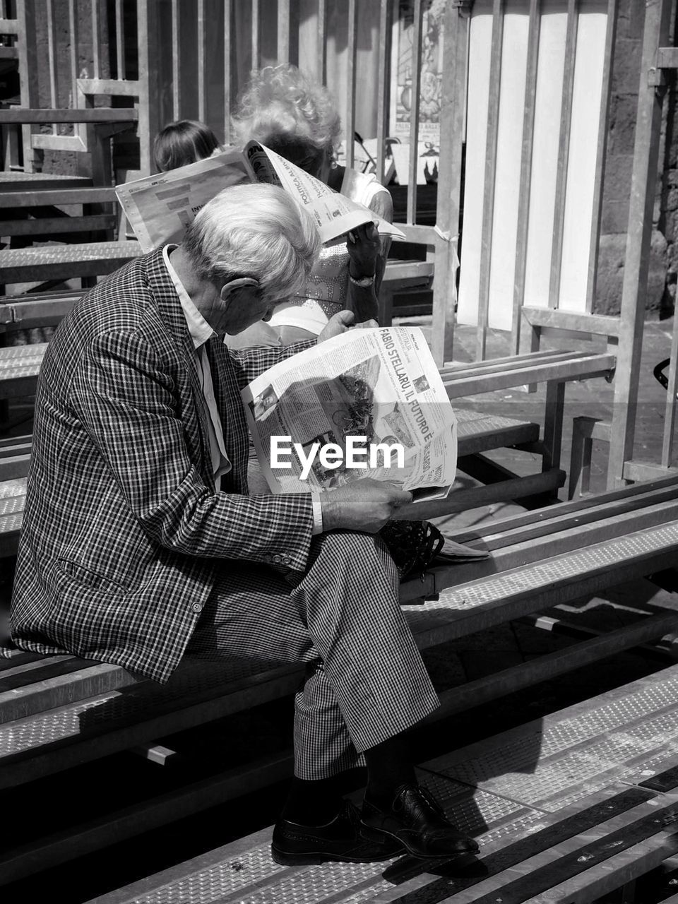 Senior man reading newspaper on bench outdoors