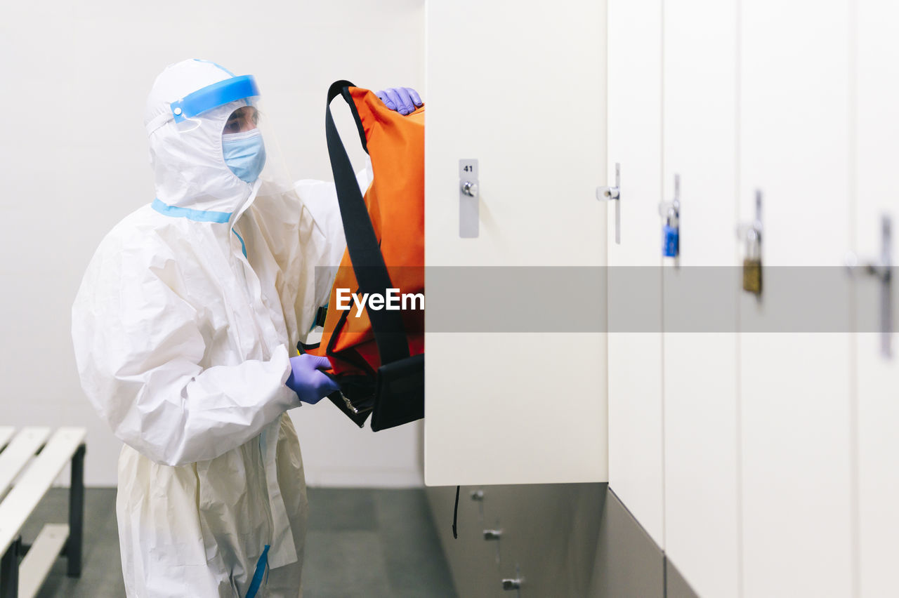 Mid adult man with protective suit removing bag from locker in hospital