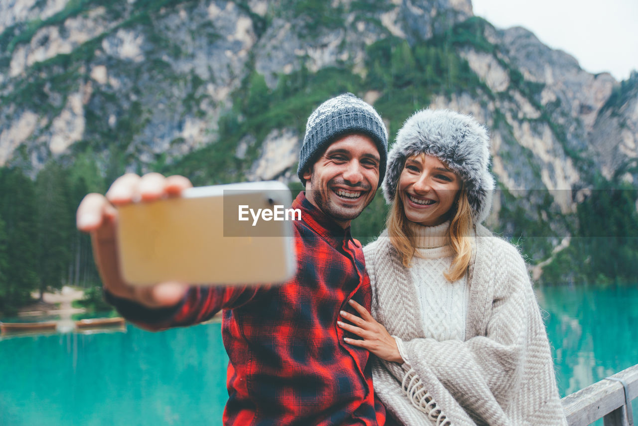 Smiling man taking selfie with girlfriend standing by lake