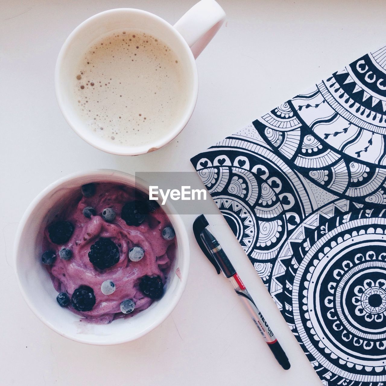 High angle view of berry yogurt with coffee cup and note pad on table