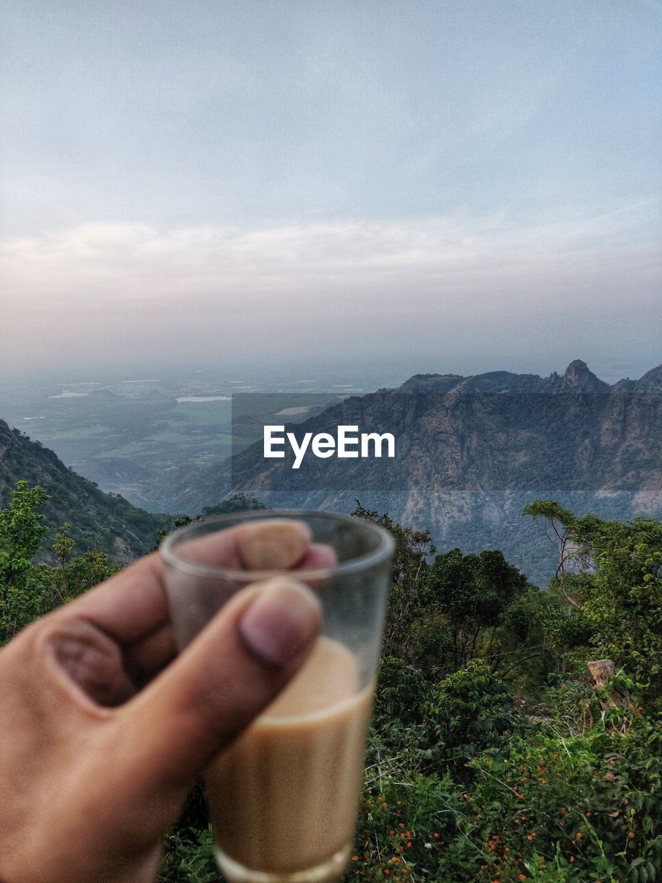 MIDSECTION OF MAN HOLDING GLASS AGAINST MOUNTAINS