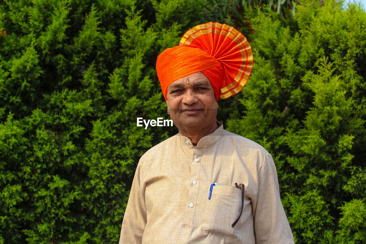 Portrait of senior man in turban standing against trees