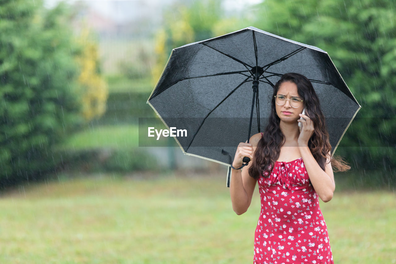 umbrella, rain, wet, protection, fashion accessory, women, one person, security, nature, adult, summer, emotion, holding, happiness, plant, grass, parasol, environment, smiling, young adult, outdoors, clothing, storm, standing, water, dress, portrait, cute, female, monsoon, cheerful, pink, drop, sheltering, fashion, lifestyles, child, front view, rainy season, positive emotion, tree, land, enjoyment, day, looking, beauty in nature, focus on foreground, relaxation
