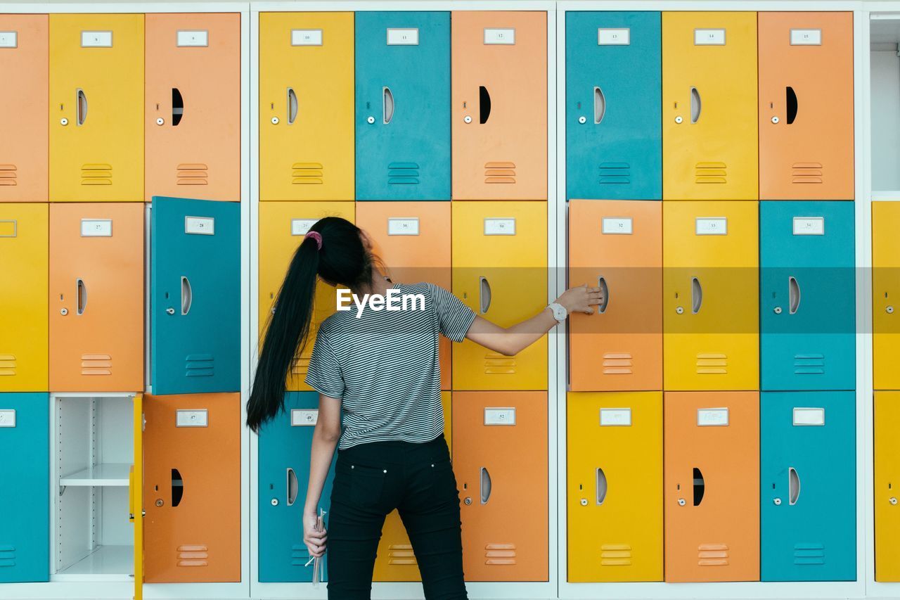 Rear view of young woman against multi colored lockers