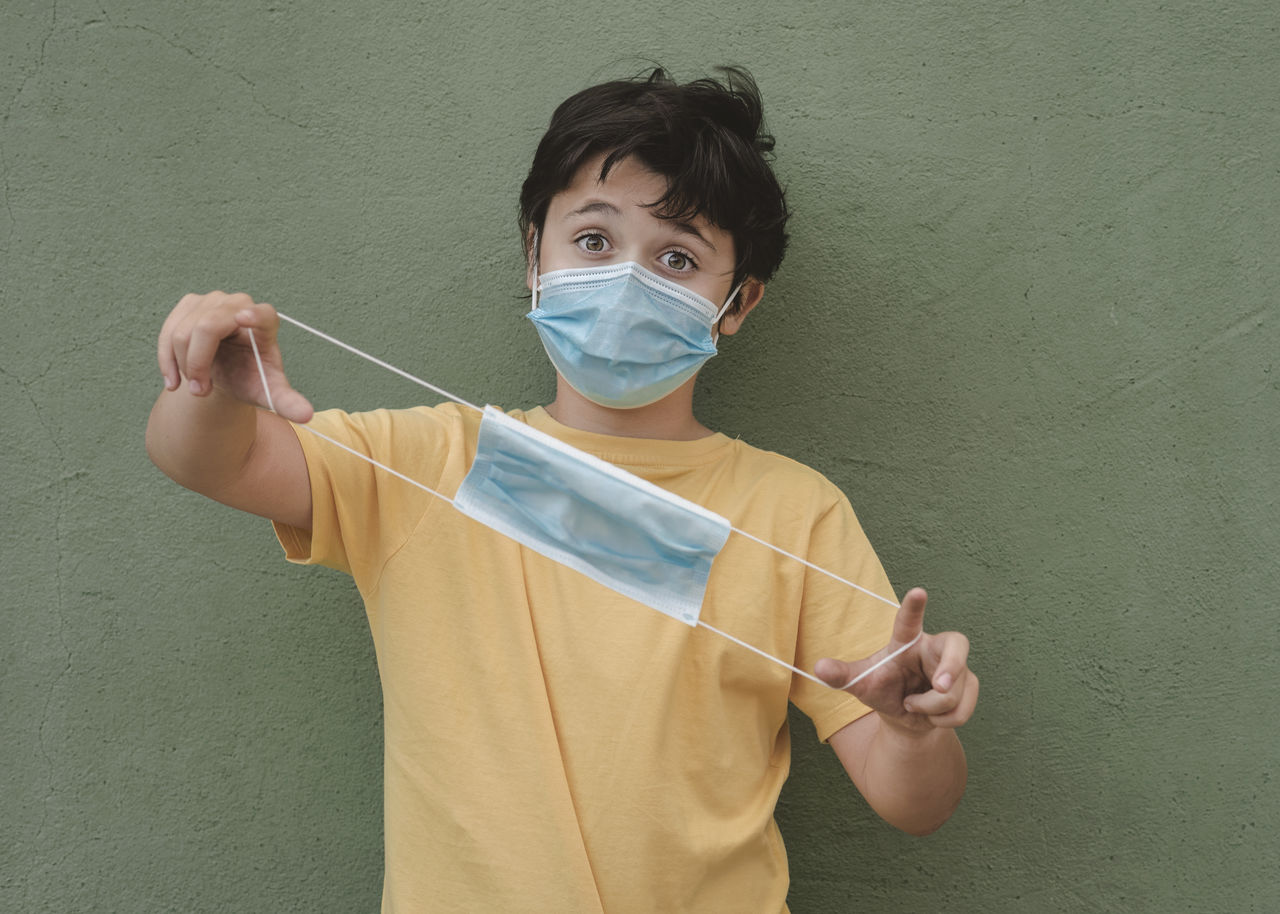 Portrait of boy holding surgical mask against wall