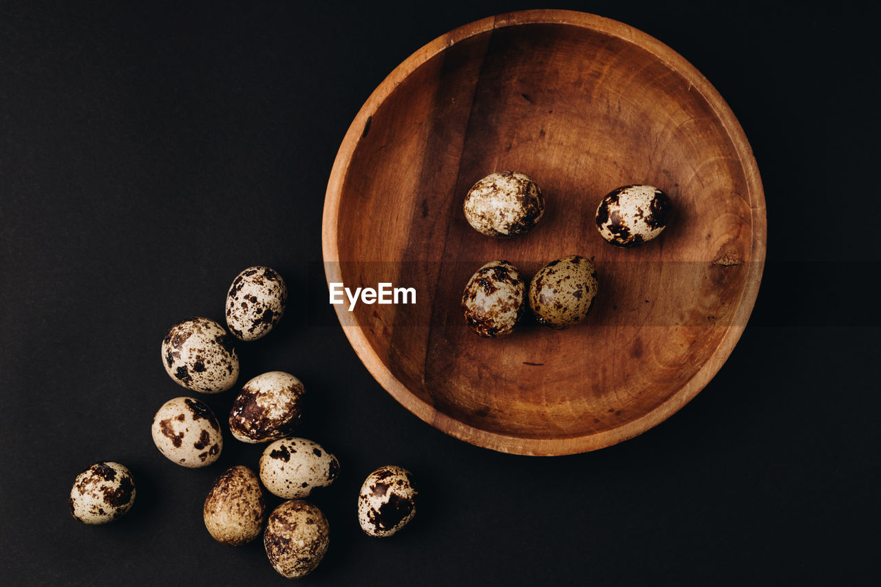 Minimal art of fresh quail eggs in the wooden bowl on the dark background.