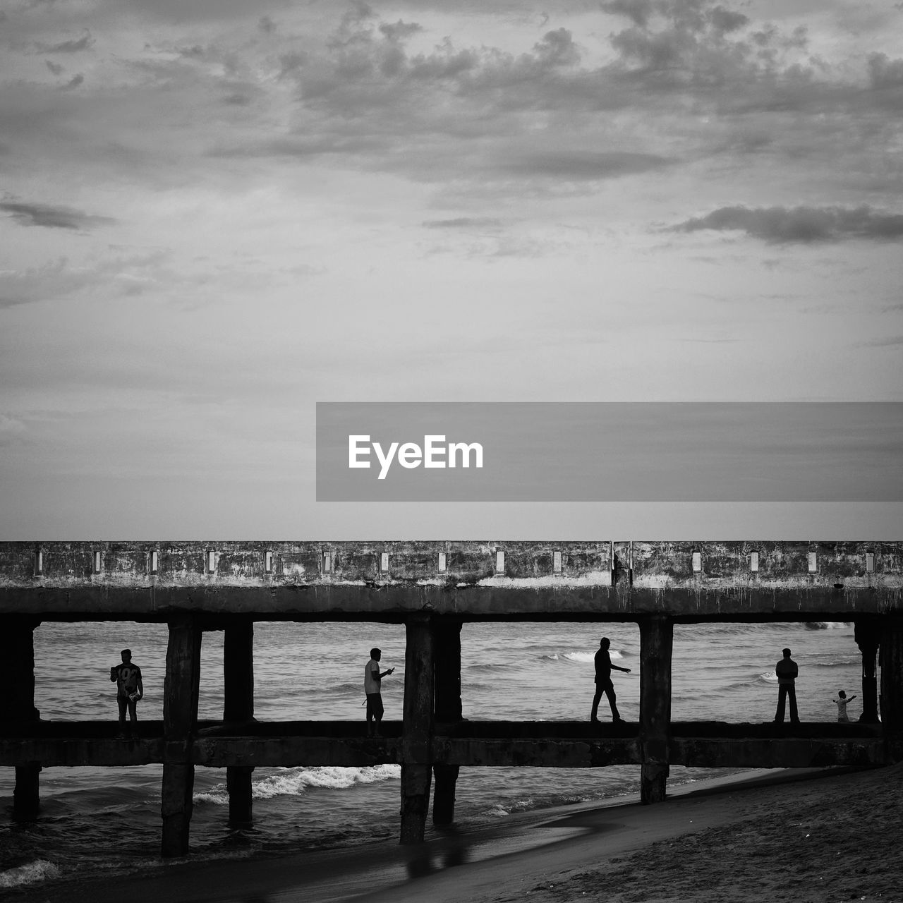 Silhouette people on pier at beach against sky