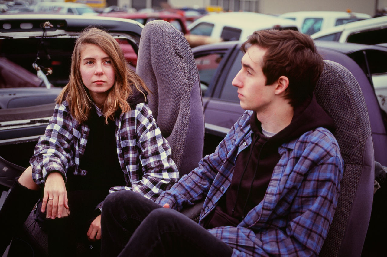 Young couple sitting in remains of a car in an auto salvage yard