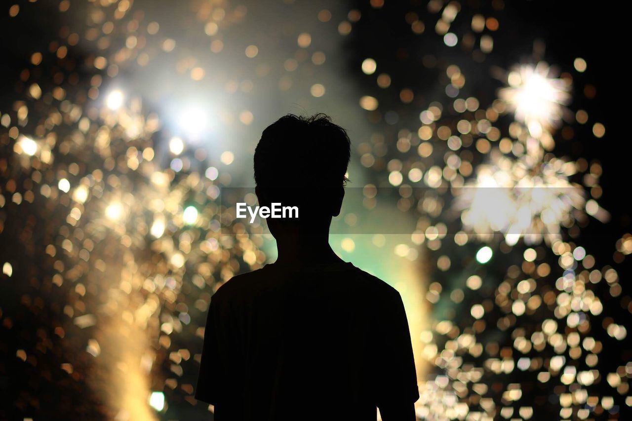 Rear view of silhouette man against illuminated sparklers at night