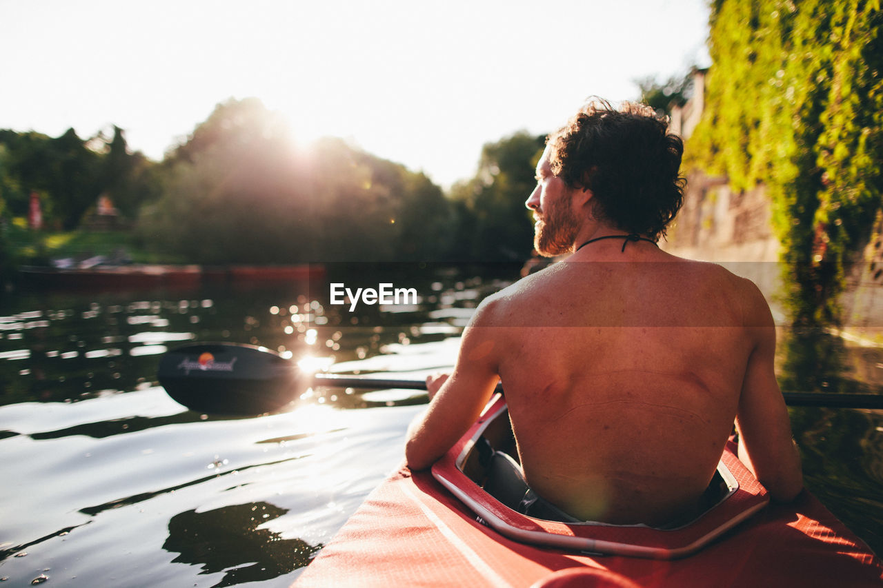 Rear view of shirtless man kayaking on river