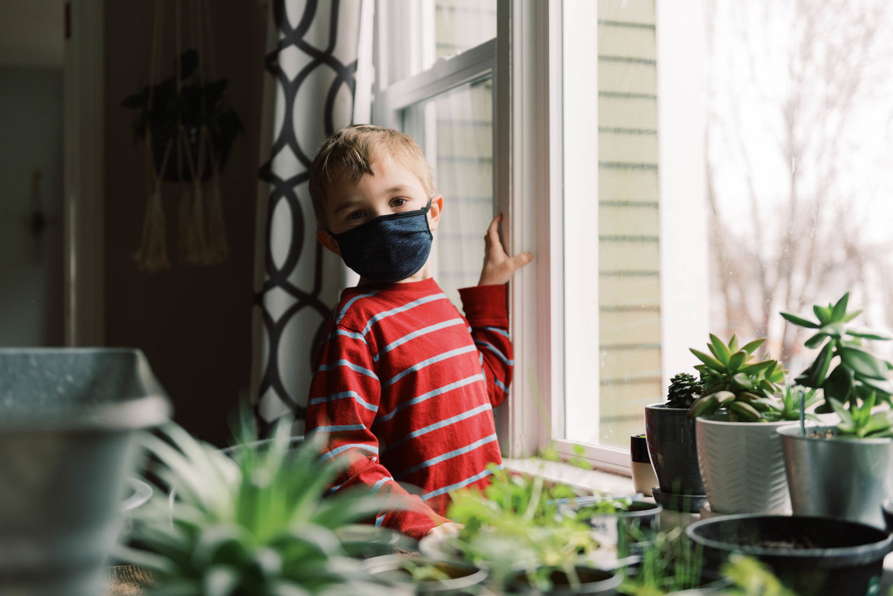 BOY STANDING BY POTTED PLANTS ON TABLE