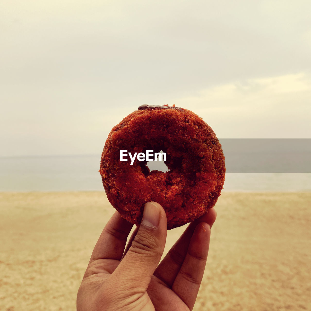 Close-up of hand holding a piece of donut on the beach