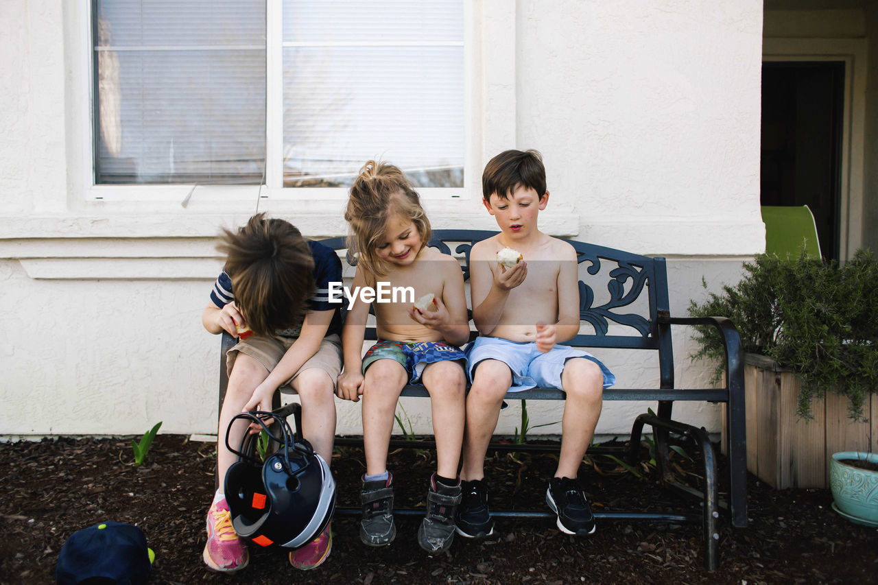Siblings eating apples while sitting on bench in backyard
