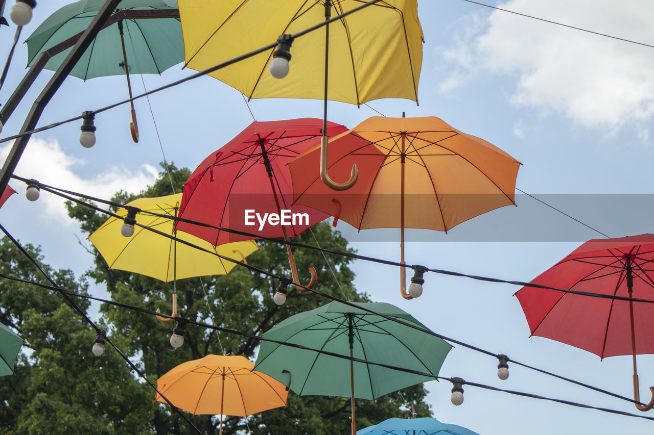 LOW ANGLE VIEW OF MULTI COLORED UMBRELLAS HANGING ON TREE AGAINST SKY