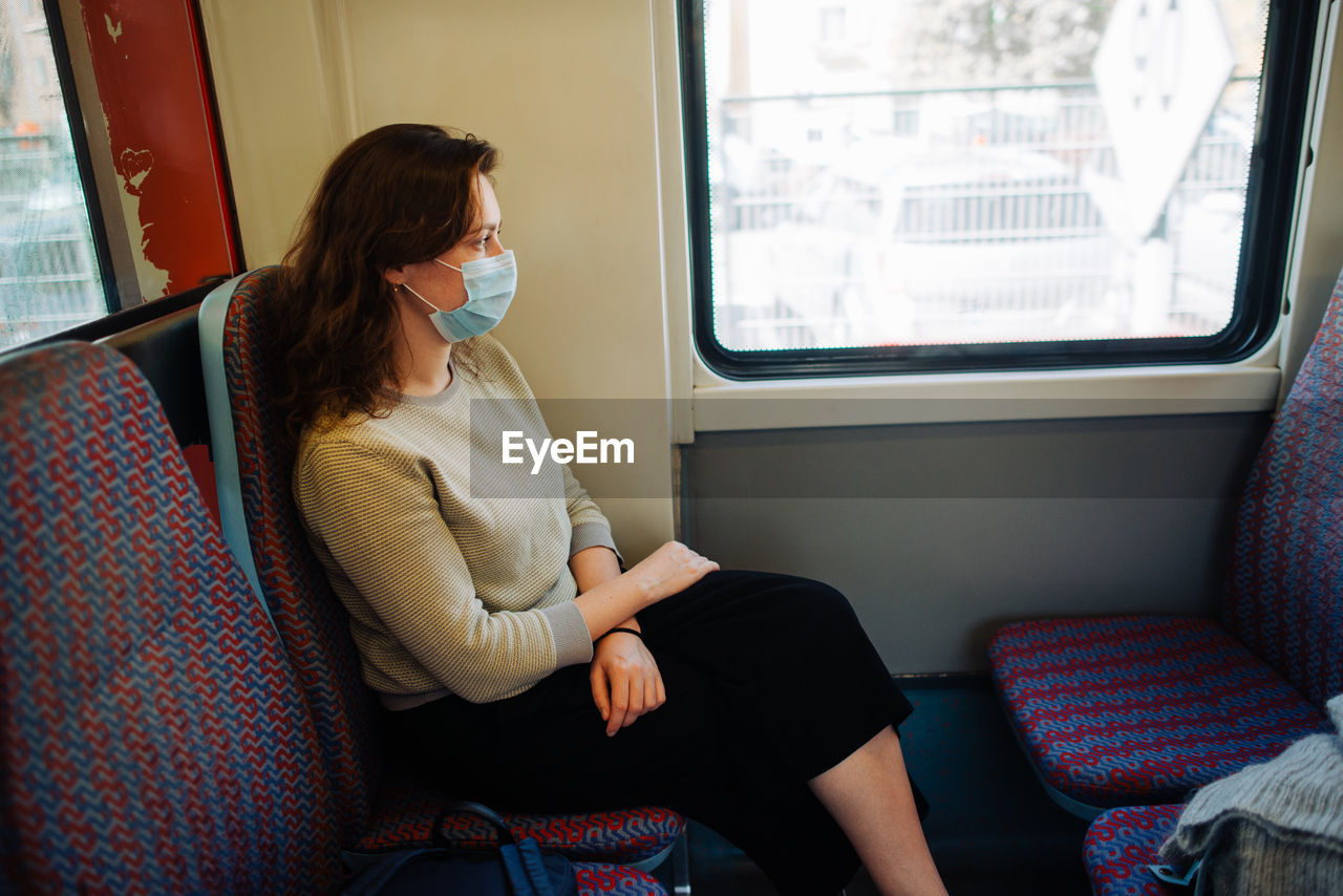 REAR VIEW OF WOMAN SITTING ON TRAIN WINDOW