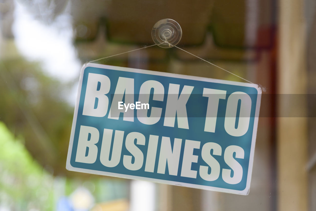 Close-up on a blue closed sign in the window of a shop displaying the message back to business.