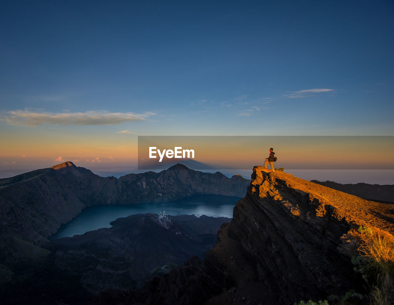 Side view of hiker standing on mountain peak against sky during sunset