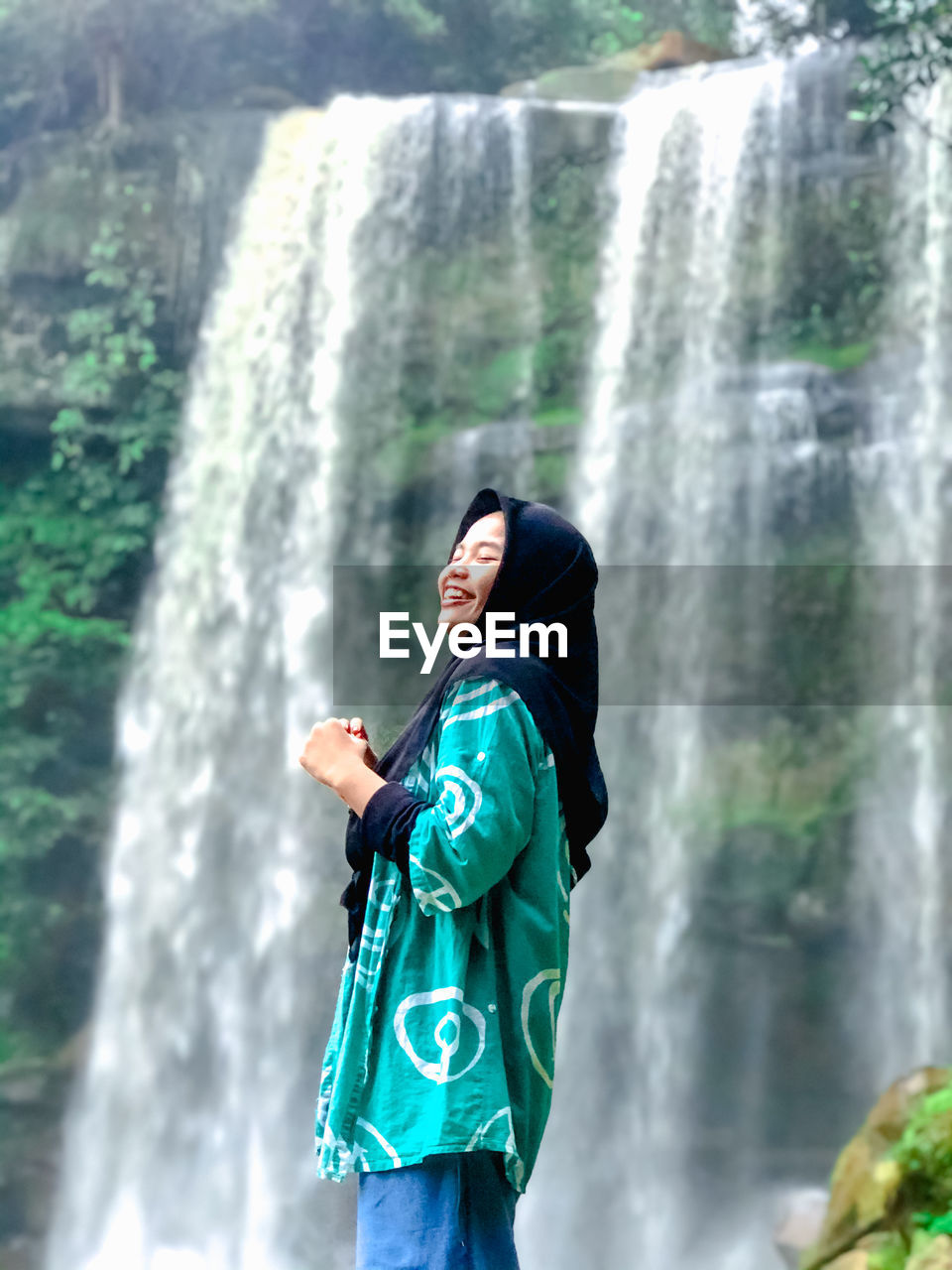 Smiling woman in hijab standing against waterfall