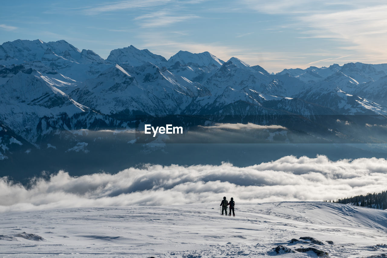 Rear view of people standing on snow covered land against mountain