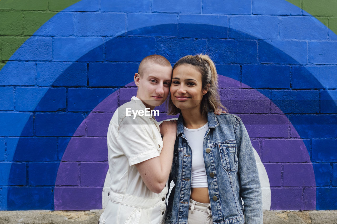 Lesbian couple standing together in front of colorful wall