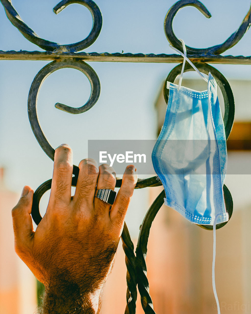 Close-up of hand holding grill and hanging mask against blue sky