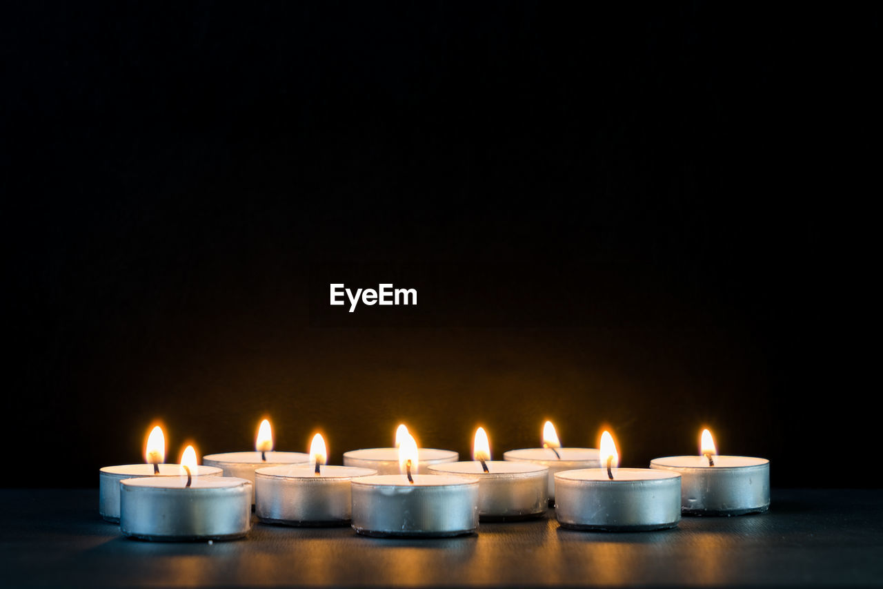Close-up of candles burning on table against black background