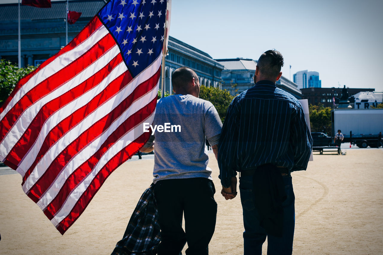 Rear view of gay couple holding hands and walking with american flag