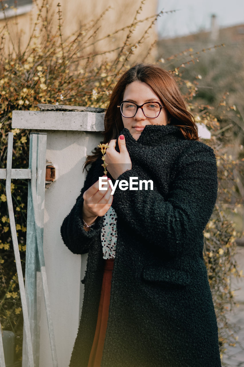 Portrait of beautiful woman standing against wall during winter