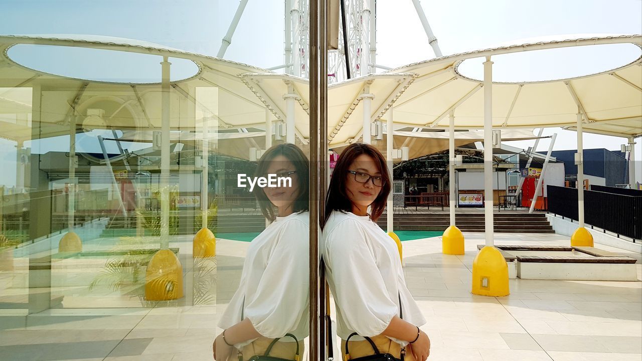 PORTRAIT OF SMILING YOUNG WOMAN STANDING ON GLASS