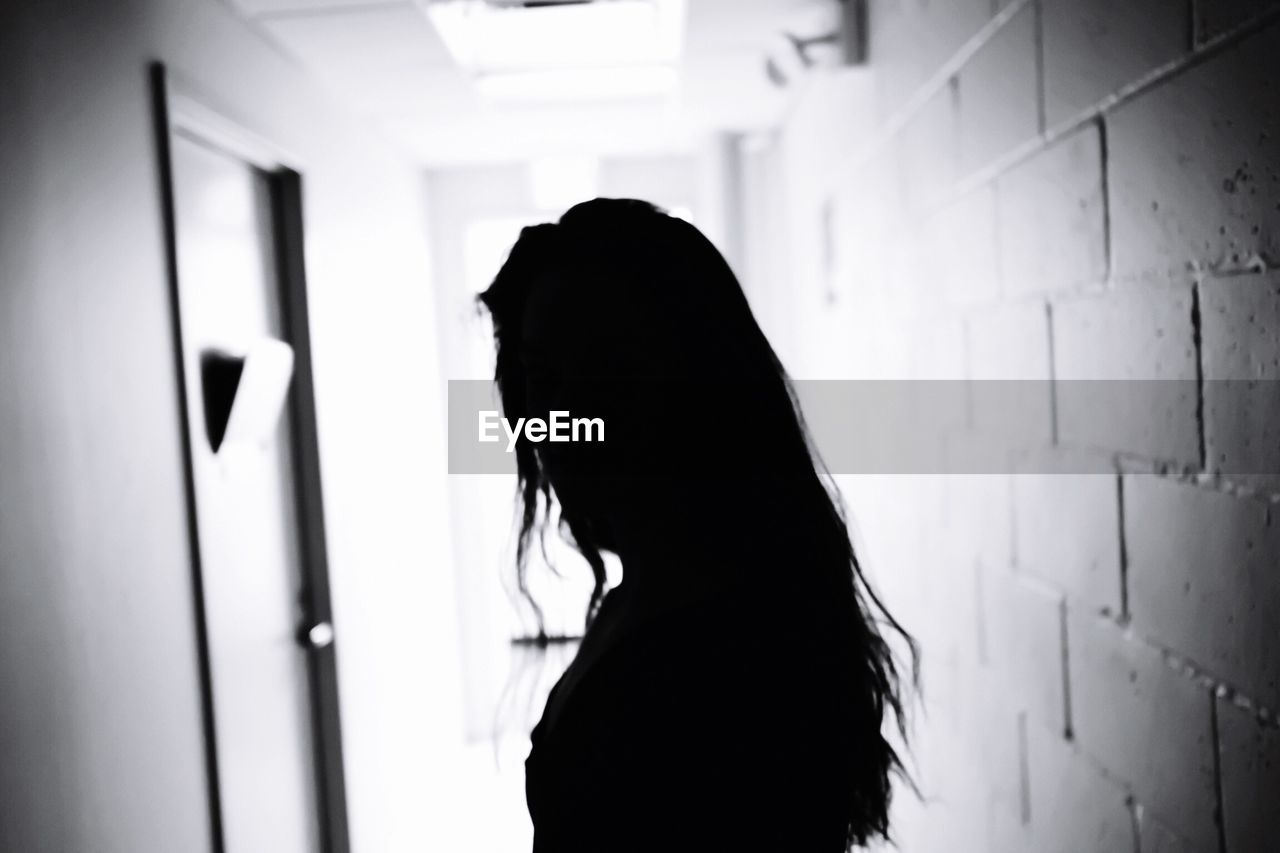 Silhouette woman standing in corridor with brick wall