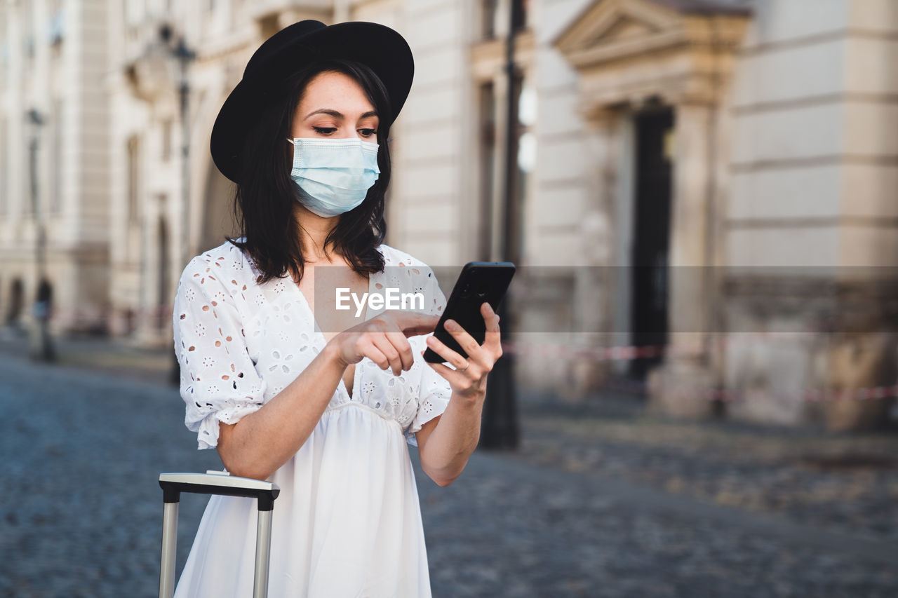 Woman wearing mask using smart phone standing on road