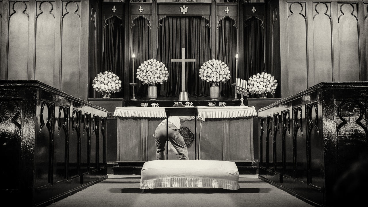 Rear view of man praying to cross while standing at altar