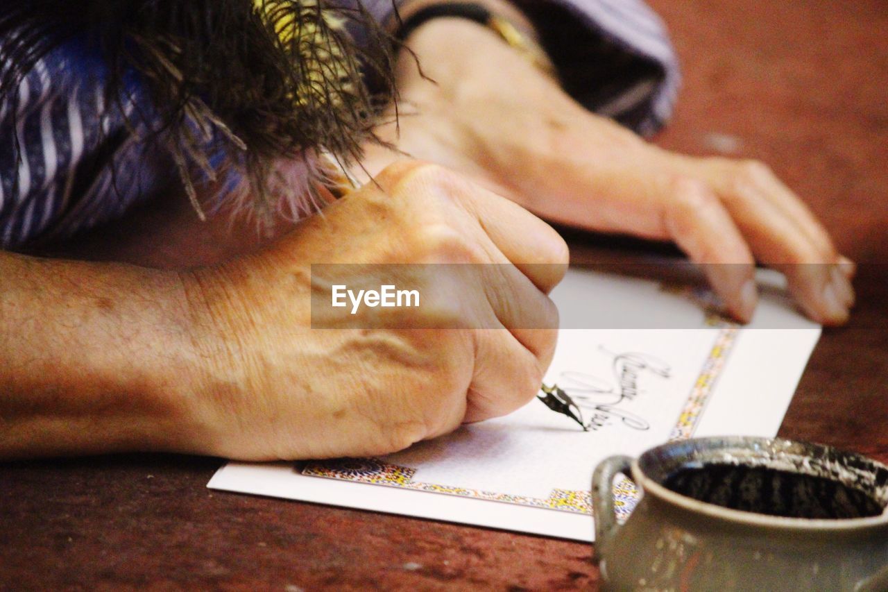 Cropped image of woman writing on paper with fountain pen on table