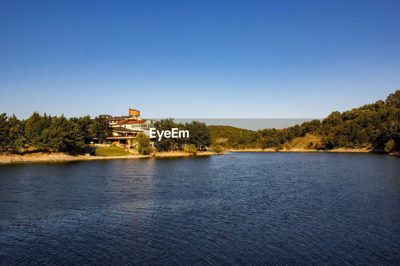 Scenic view of lake by building against clear blue sky